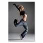 Preview: Blonde Tänzerin in Jeans und bauchfreiem Top springt mit ausgestrecktem Bein und Arm.