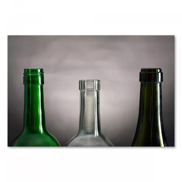 Drei leere Glasflaschen in grün, klar und dunkelgrün stehen nebeneinander vor einem grauen Hintergrund. Drei leere Glasflaschen in grün, klar und dunkelgrün stehen nebeneinander vor einem grauen Hintergrund.