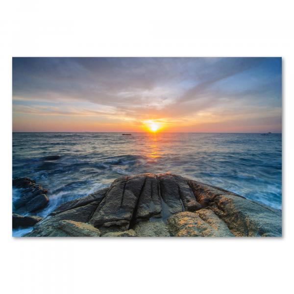 Die untergehende Sonne taucht das Meer und Felsen am Strand in ein goldenes Licht.