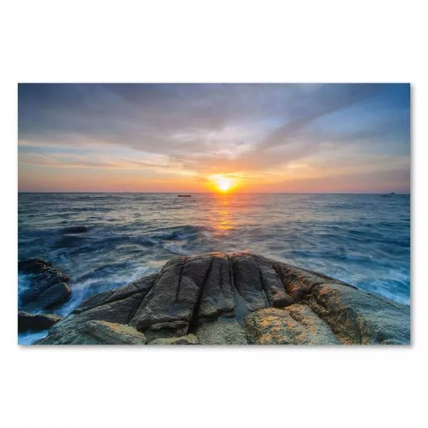 Die untergehende Sonne taucht das Meer und Felsen am Strand in ein goldenes Licht.