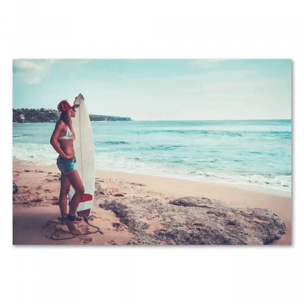 Surferin, Surfbrett, Strand, Blick aufs Meer, weißes Top, Jeans, Kappe. Surferin, Surfbrett, Strand, Blick aufs Meer, weißes Top, Jeans, Kappe.